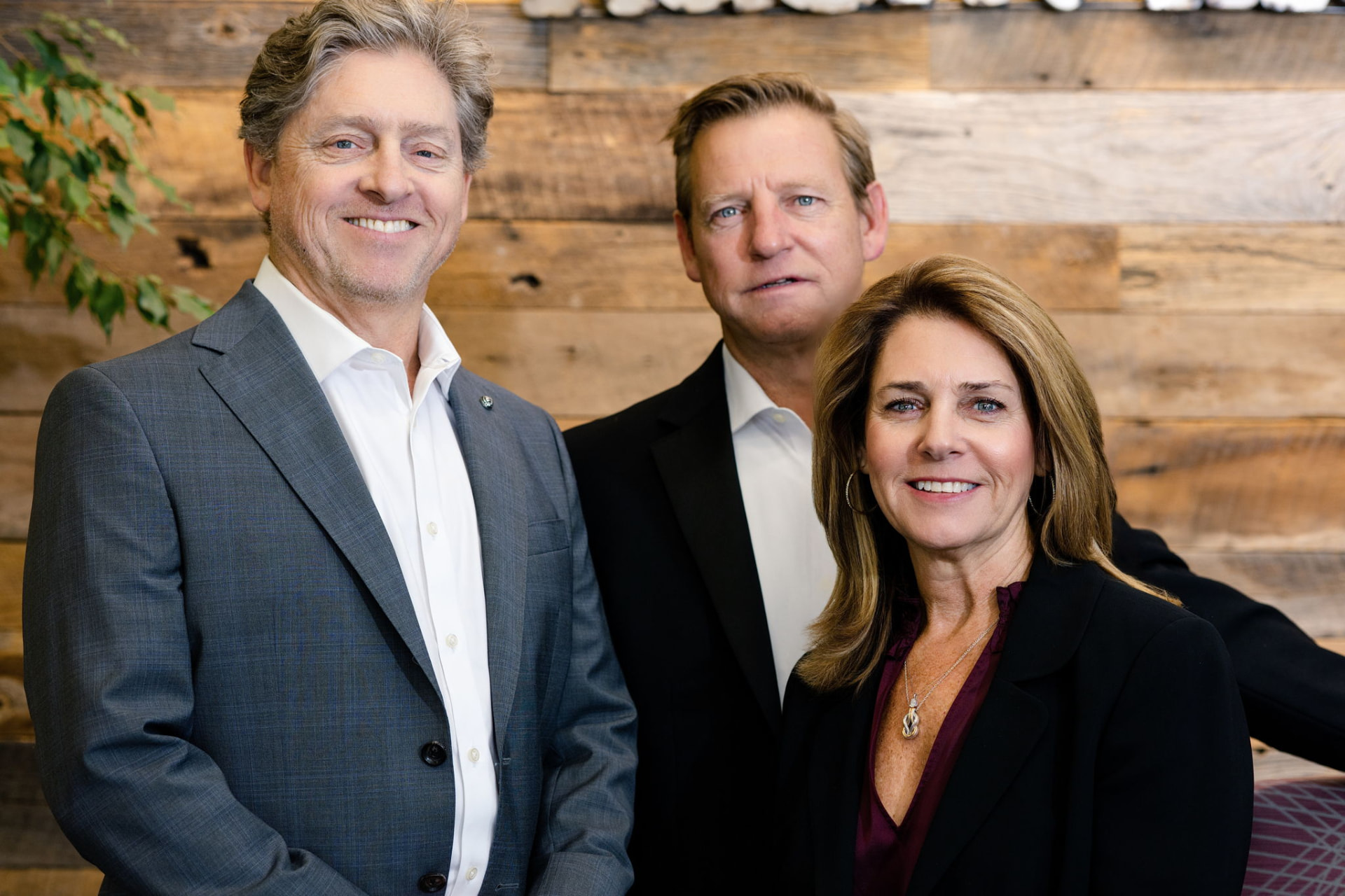 The Holmes and Pruett Homes Team, three Nashville realtors, standing together in front of a reclaimed wood wall