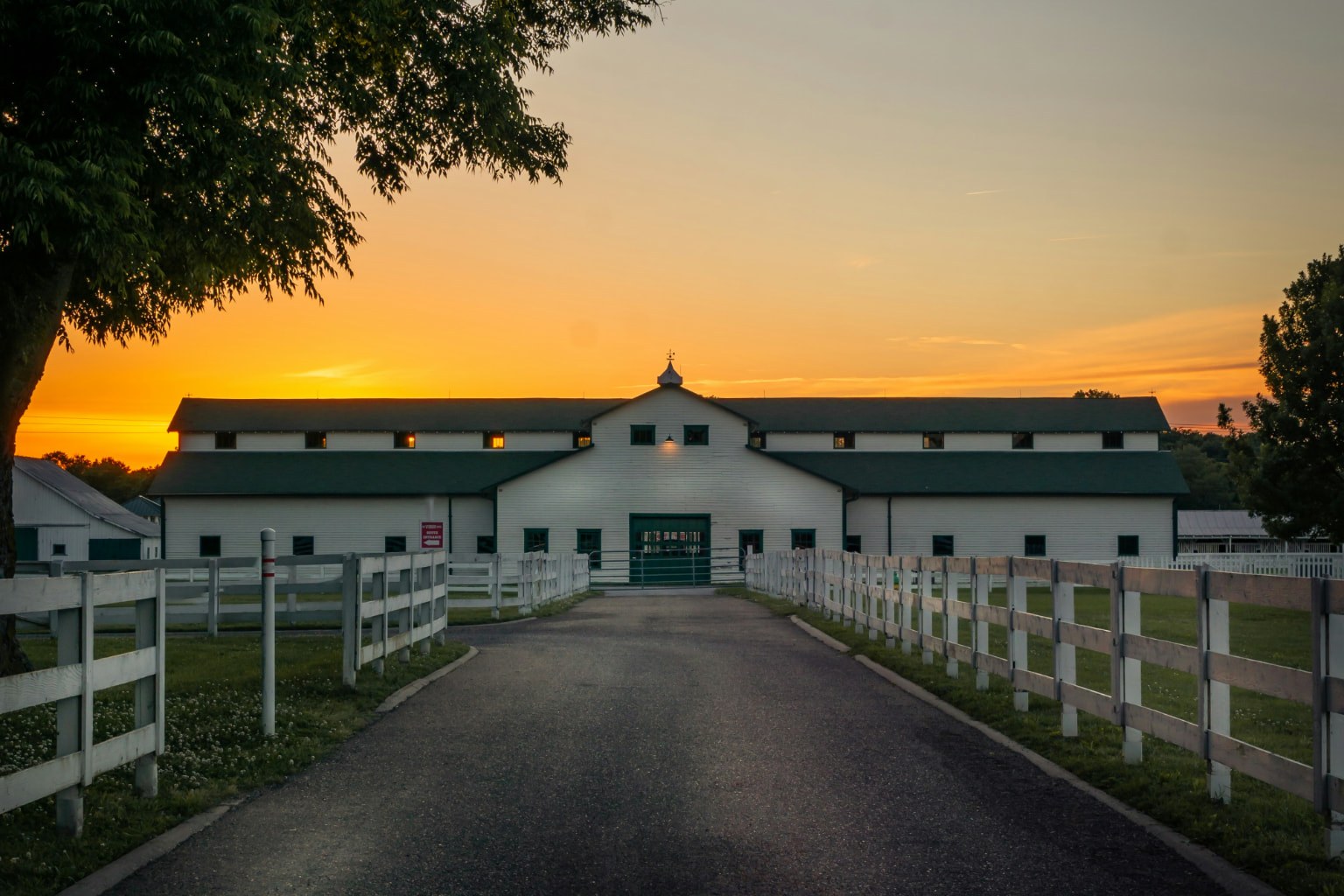 White horse barn at sunset behind a board fence near Franklin