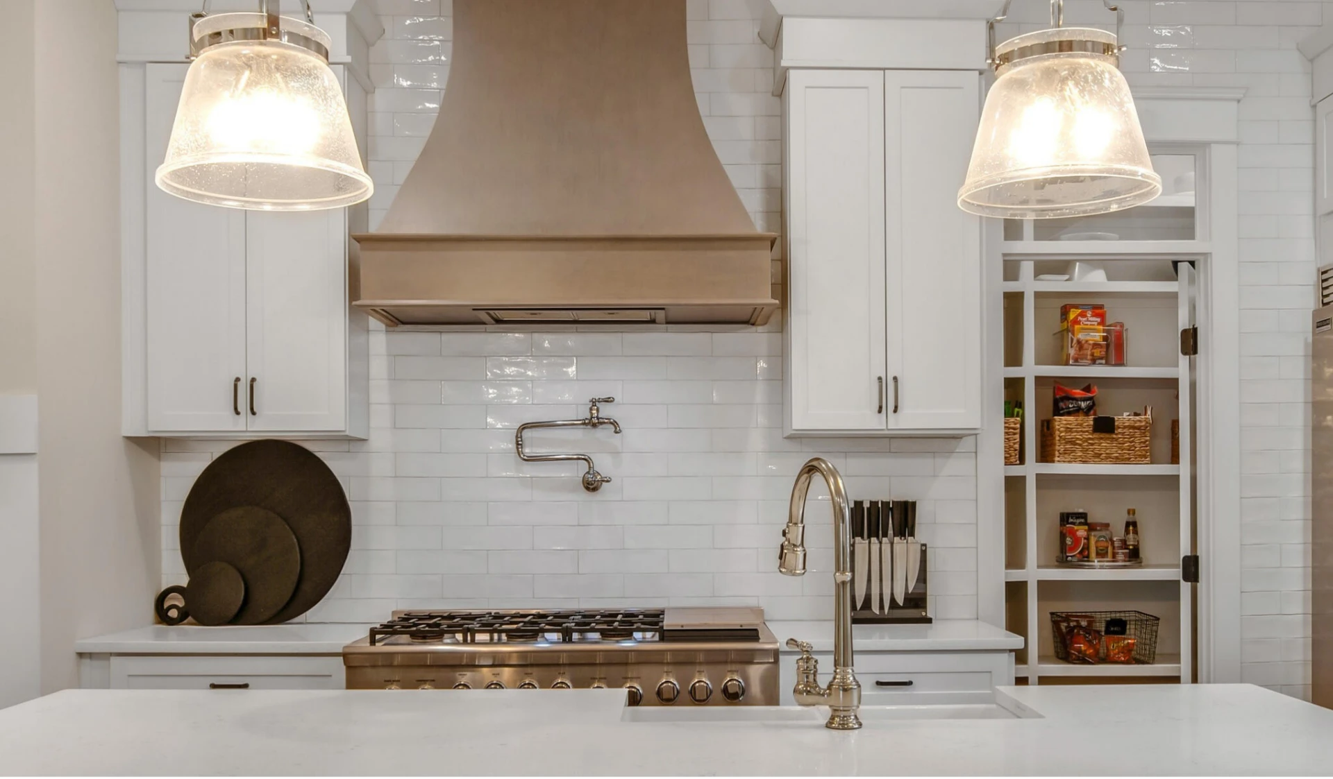 Bright white kitchen with a plaster range hood, brass fixtures and a marble island