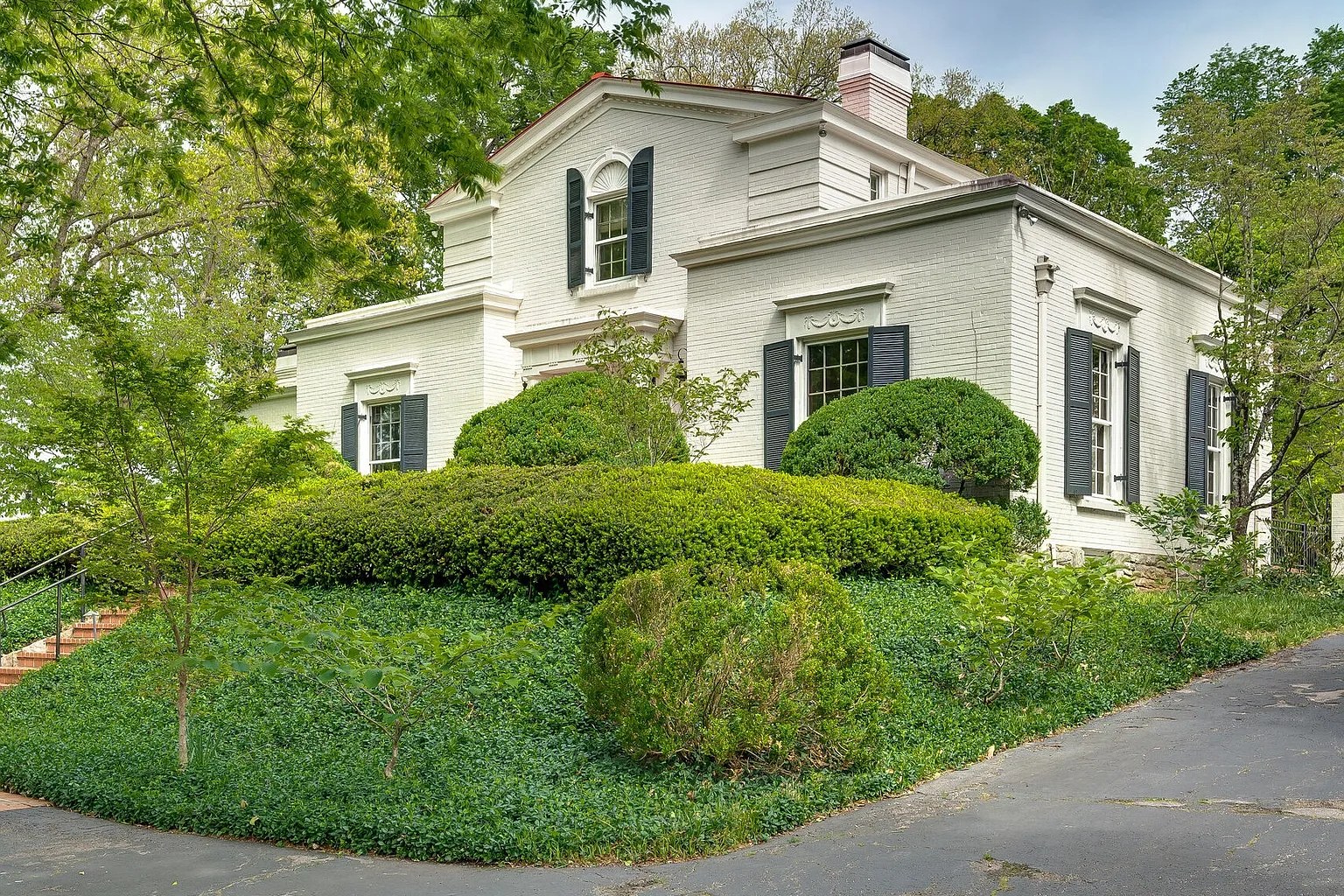 White brick home behind mature landscaping in Green Hills